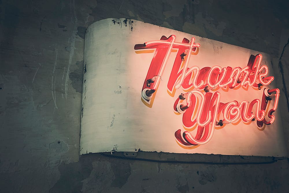 Red neon sign reading “Thank You!” mounted on a weathered wall