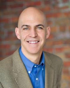 Andy Scantland, founder of Upside Partners, smiling in a tan blazer and blue shirt