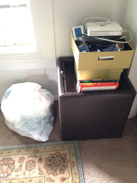 Trash bag and a bin stacked with boxes, books, and electronics waiting to be discarded