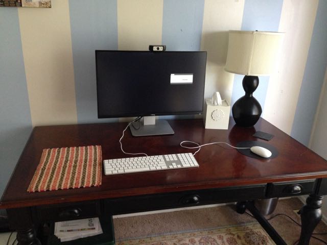 Tidy desk holding only a monitor, keyboard, mouse, and lamp against a striped wall