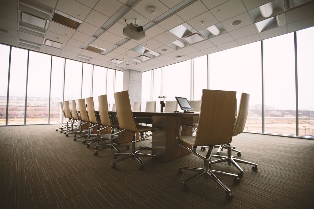 Empty conference room with a long table, rows of office chairs, a laptop, and floor-to-ceiling windows