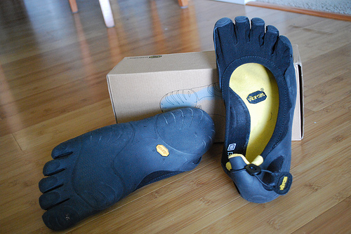 Pair of black Vibram FiveFingers shoes beside their box, one sole facing up