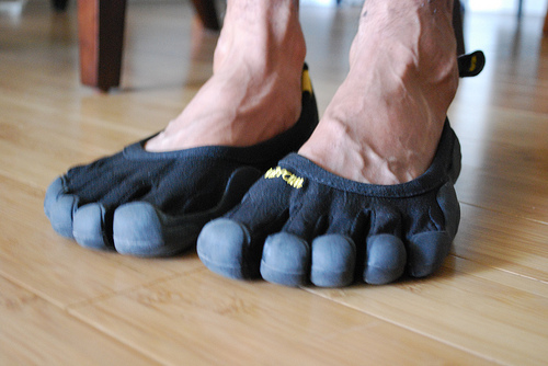 Black Vibram FiveFingers toe shoes worn on bare feet on a wood floor