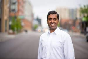 Ravi Raman smiling in a white dress shirt on a city street