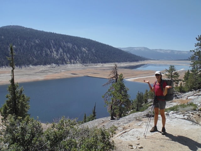 Hiker in a red shirt posing with arms spread above a half-drained mountain reservoir