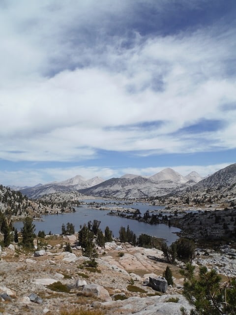 Alpine lake basin ringed by granite peaks under a towering cloudy sky