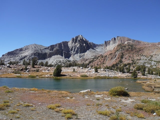 Still alpine lake below jagged granite peaks on a cloudless day