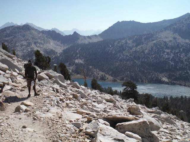 Hiker descending a white granite talus slope above a deep blue alpine lake