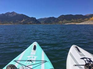 Noses of two paddleboards on a blue mountain lake with peaks and shoreline ahead