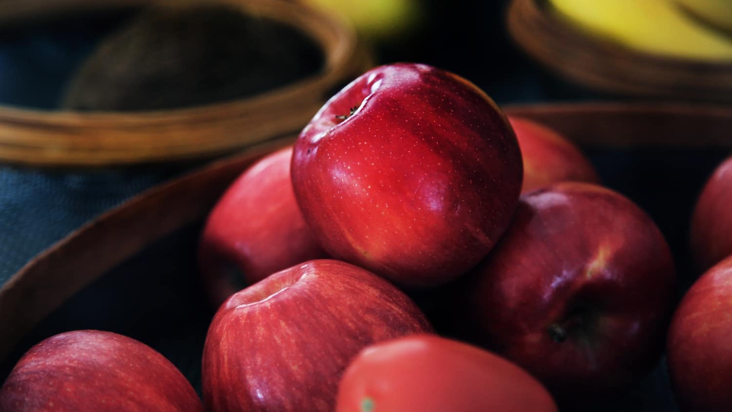 Close-up of shiny red apples piled in a dark wooden bowl