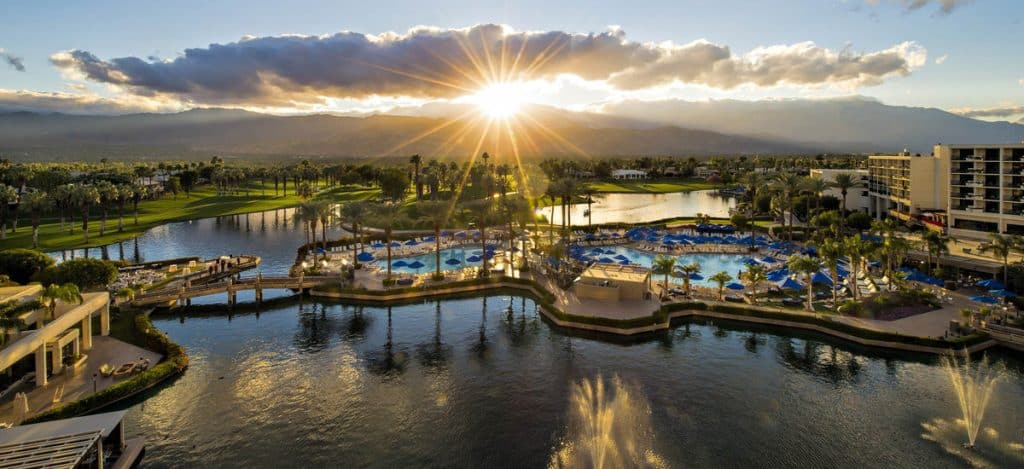 Sunburst over a palm-lined desert resort with pools and lagoons at dusk