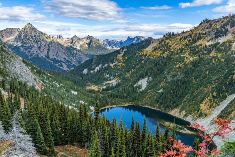 Deep blue alpine lake ringed by conifers and golden larches beneath rugged mountain peaks