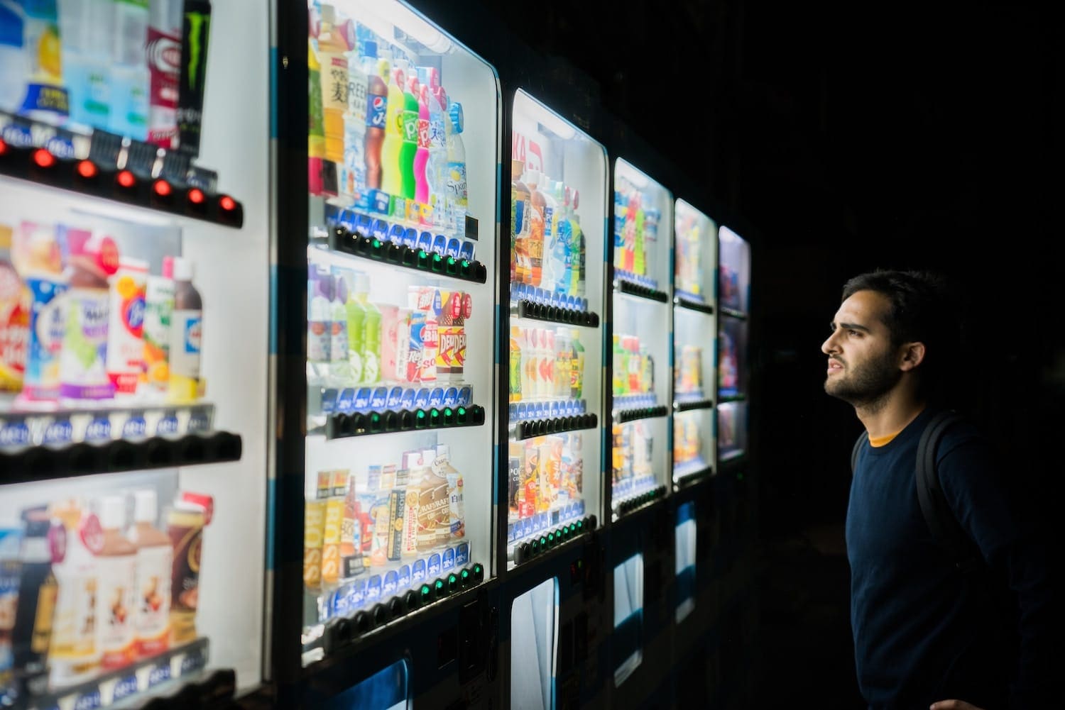 Man gazing at rows of brightly lit Japanese drink vending machines at night